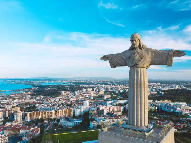 statue of Christ with a large city by the sea in the background