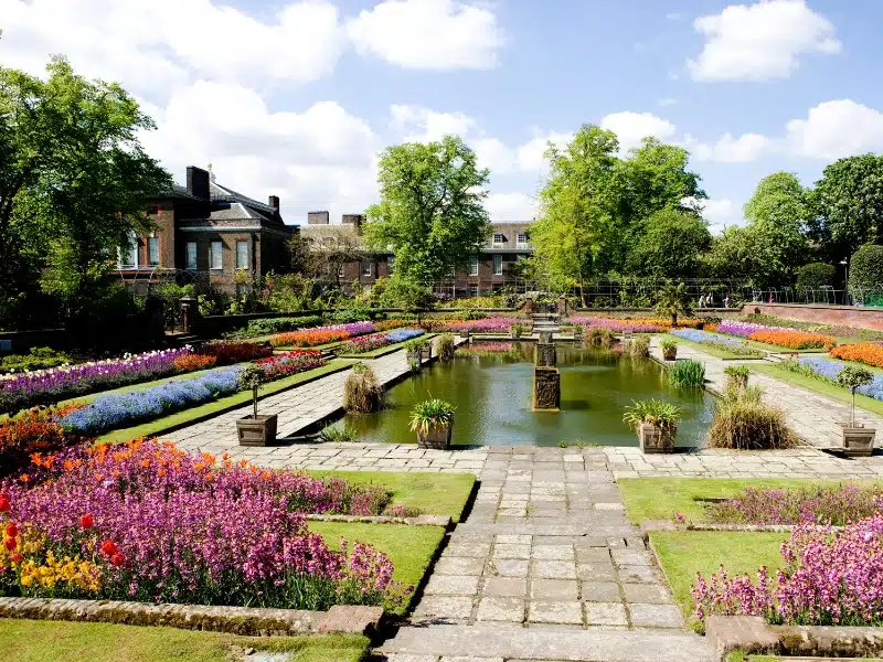 colorful flowers around an ornamental pond with a grand house in the background