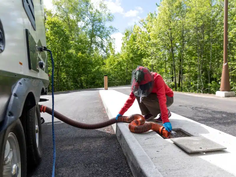 person dressed in red holding a sewage hose from a motorhome into a sewer