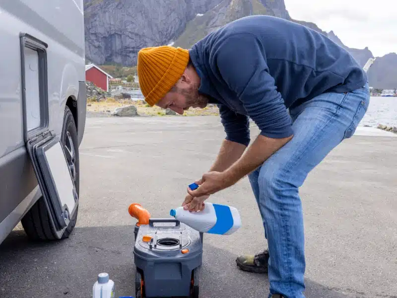 man in an orange hat cleaning a toilet cassette by a motorhome