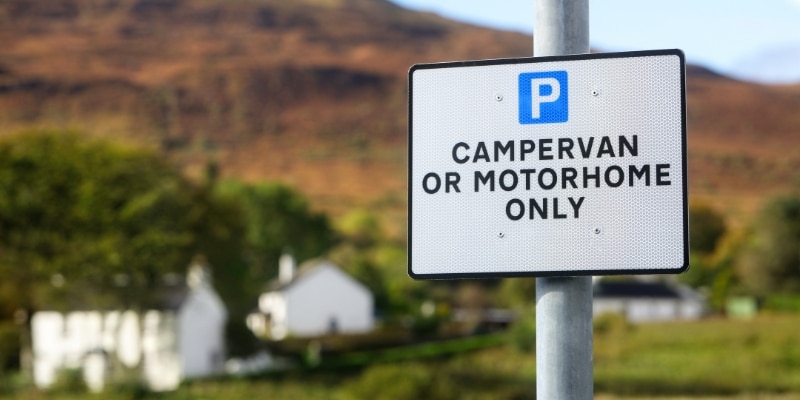 Parking sign showing 'campervan or motorhome only' with white buildings in the background