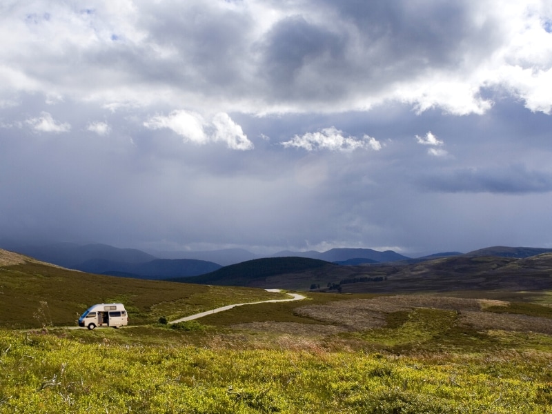 a silver campervan parked alongside a track surrounded by grasses and heather