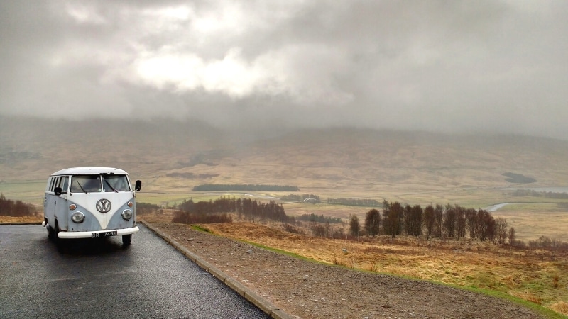 a grey VW campervan parked overlooking a valley of autumn heather