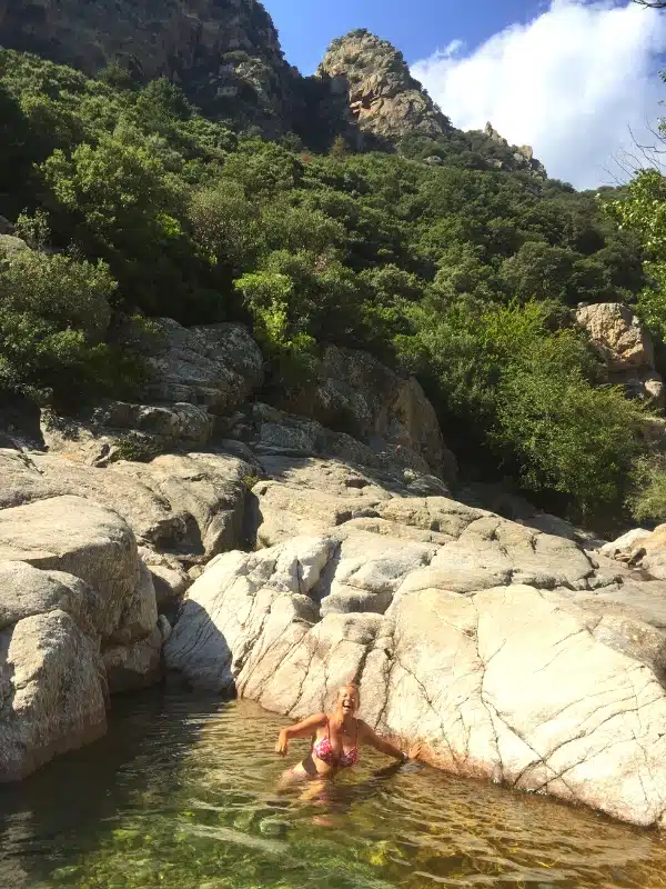 woman in a red bikini in a small natural pool surrouned by boulders and trees