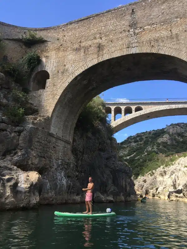 man on a paddle board underneath an arched stone bridge