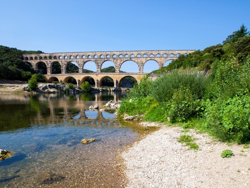 multi-arched bridge over a clear pebbly river surrouned by vegetation