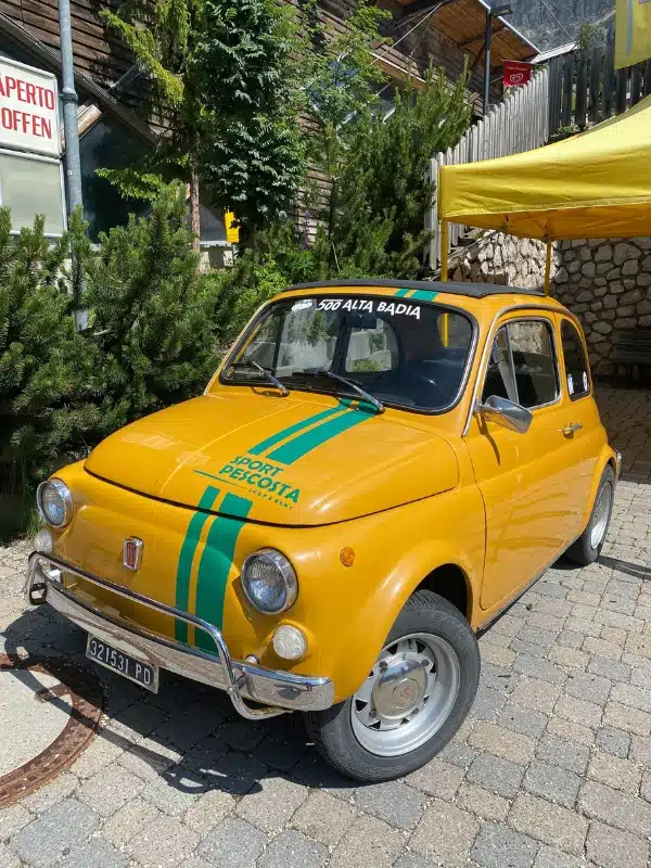 yellow and green classic Fiat 500 parked by a stone wall