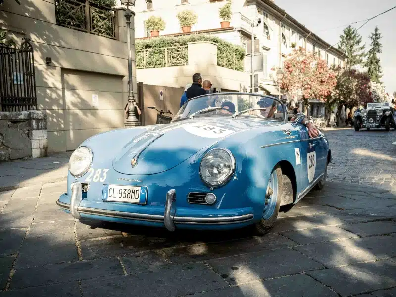 blue classi Porsche car on a cobbled road with two drivers in the car