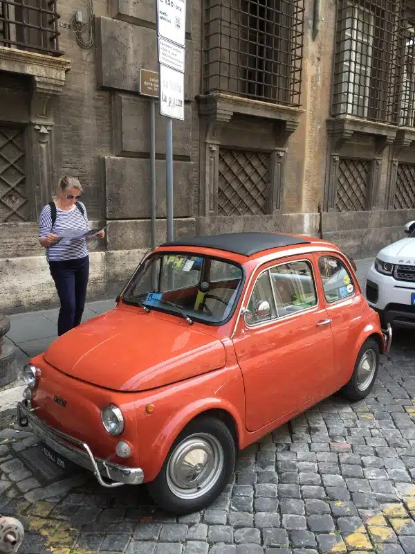red Fiat 500 with a woman in a striped top standing next to it looking at a map