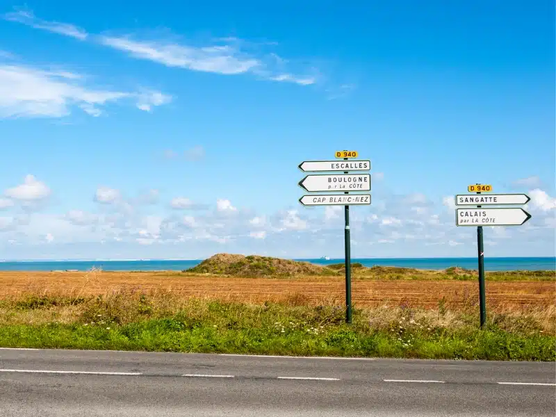 French road signs against a backdrop of fields and sea