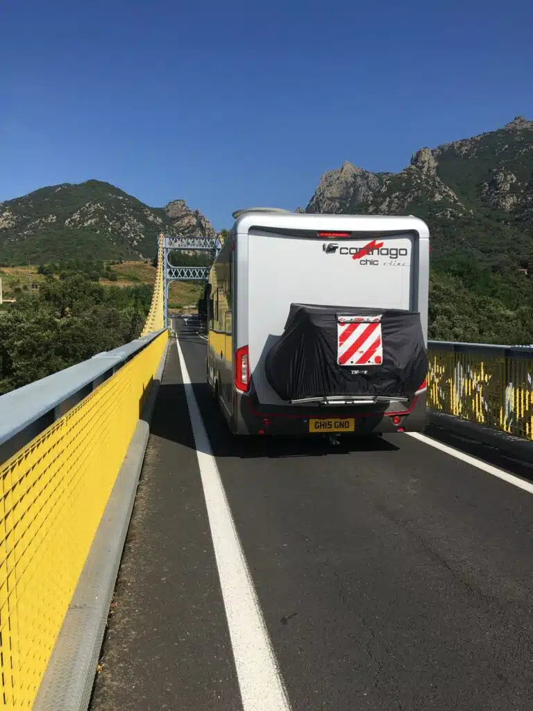 large silver motorhome crossing a single track bridge with yellow and grey ironwork