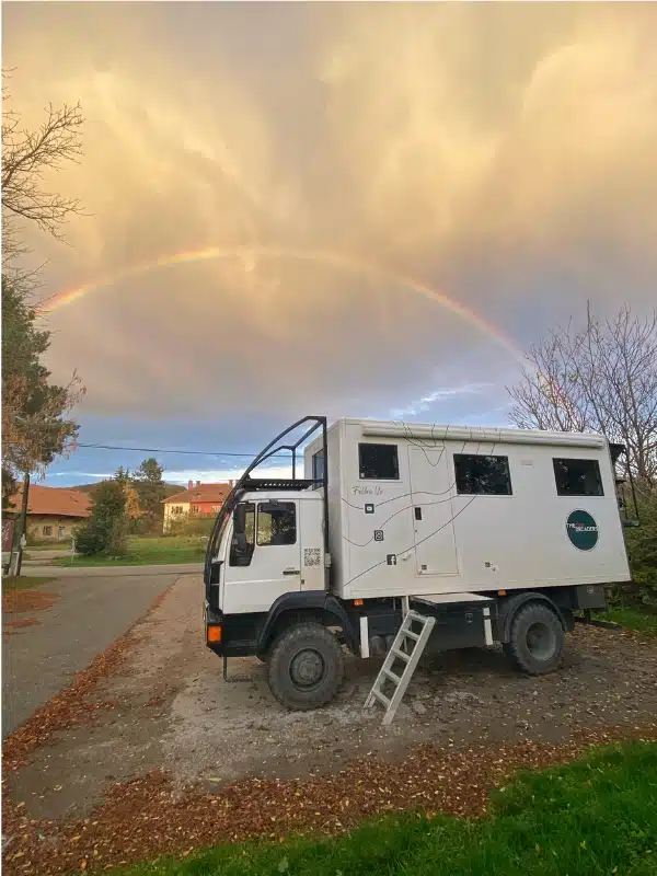 overland truck parked in a small car park with a double rainbow