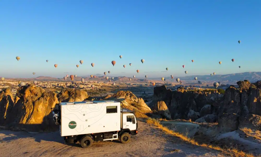 overland truck parked in a valley in Capadoccia with many hot air baloons taking off in the background