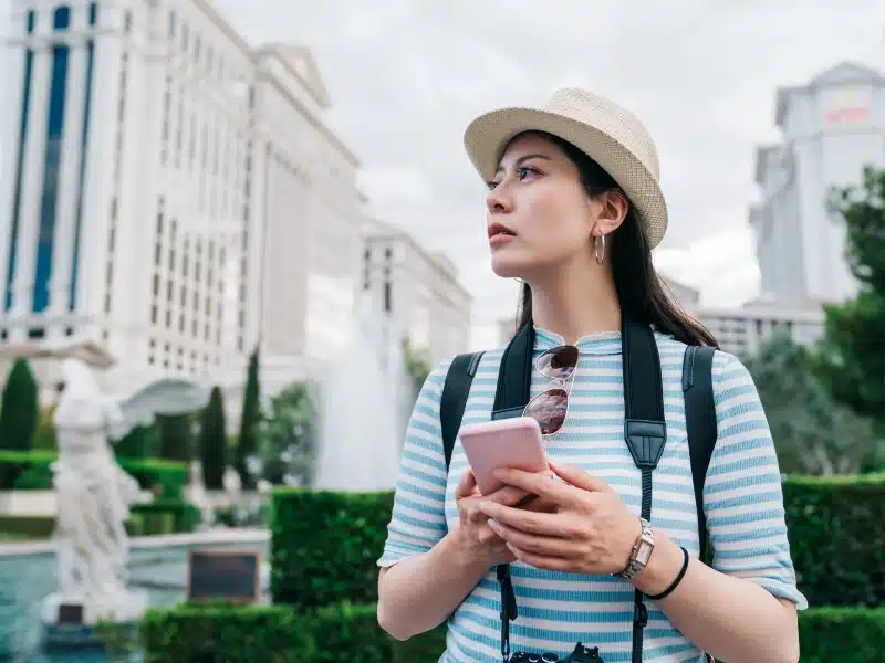 Woman wearing a straw hat and blue and white striped t-shirt in a city using a phone in a pink case
