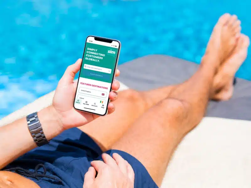 person using a mobile phone sitting on a sun lounger by a swimming pool