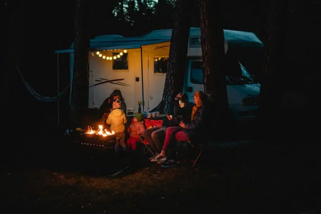 motorhome at night with fairy lights on and a family around a fire pit
