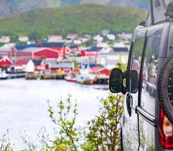 campervan parked up facing water and a village of red and white buildings