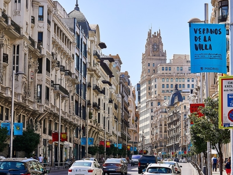 a busy sstreet lined with tall creamy colored buildings abd cars on the road