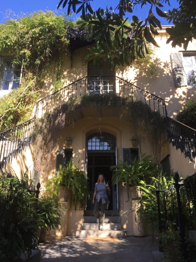 woman on the steps of a creamy coloured building drapes with green vines and plants