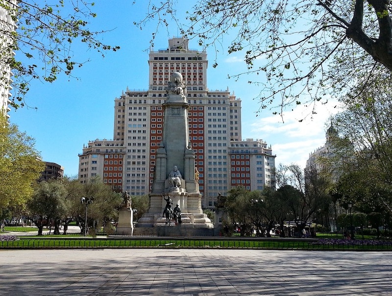 leafy square with a large building and many statues