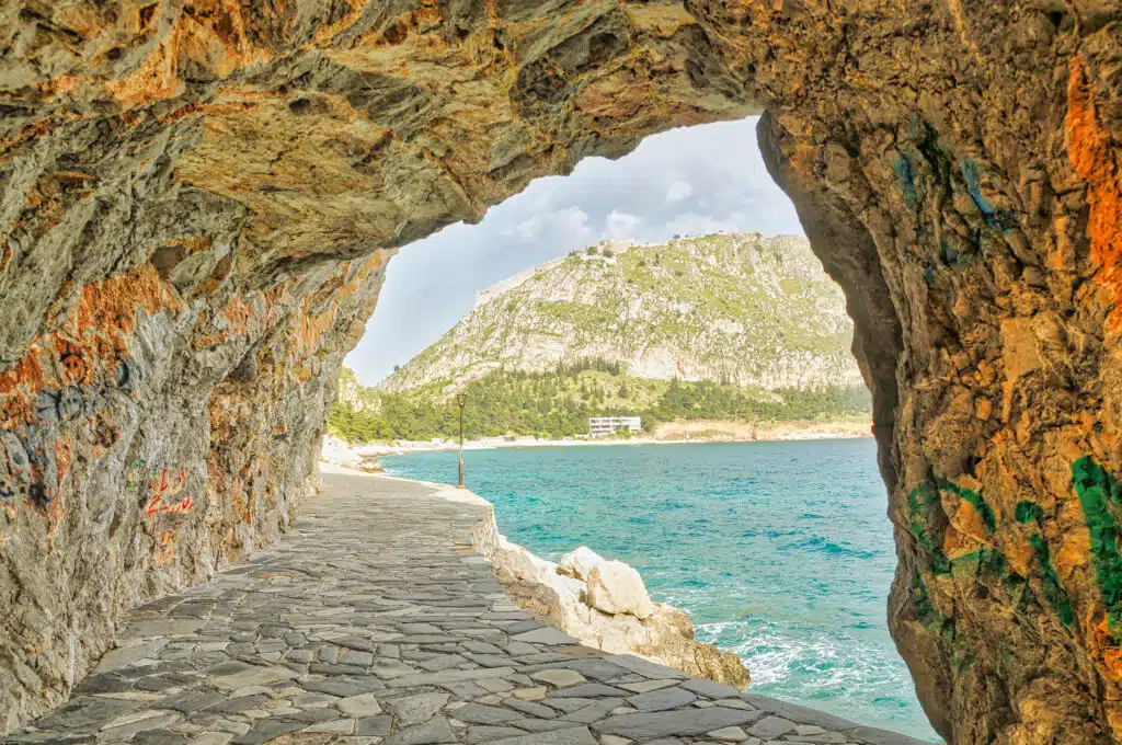 large rocky arch over a paved path by the sea