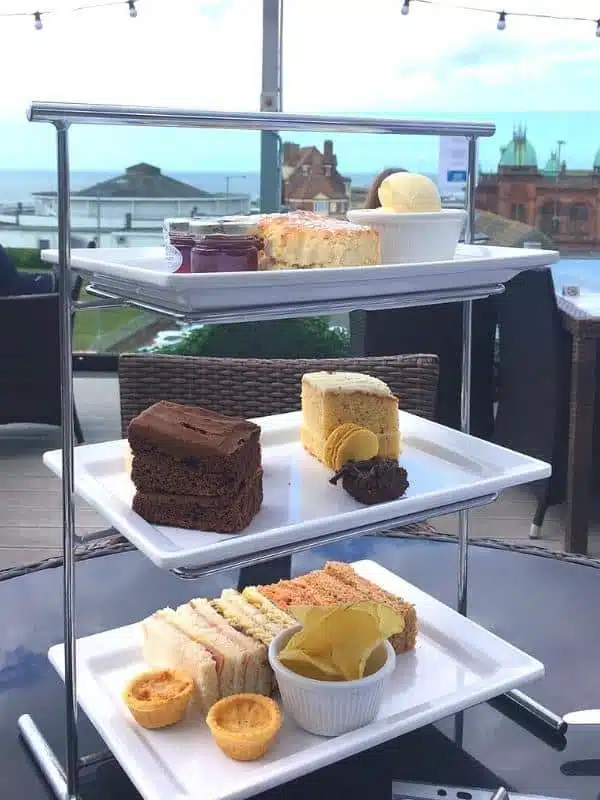 oblong plates of cakes and sandwiches set on a table overlooking an English seafront