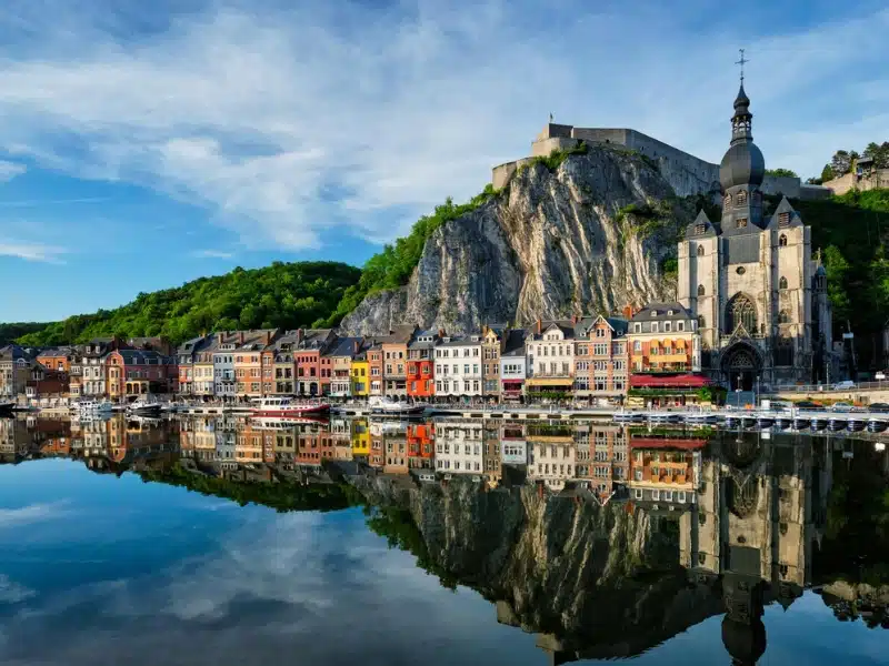 colorful houses and an onion domed church along a river with a high cliff backdrop