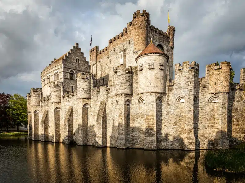 Large stone castle with round turreted towers and a main crenellated building surrounded by a moat