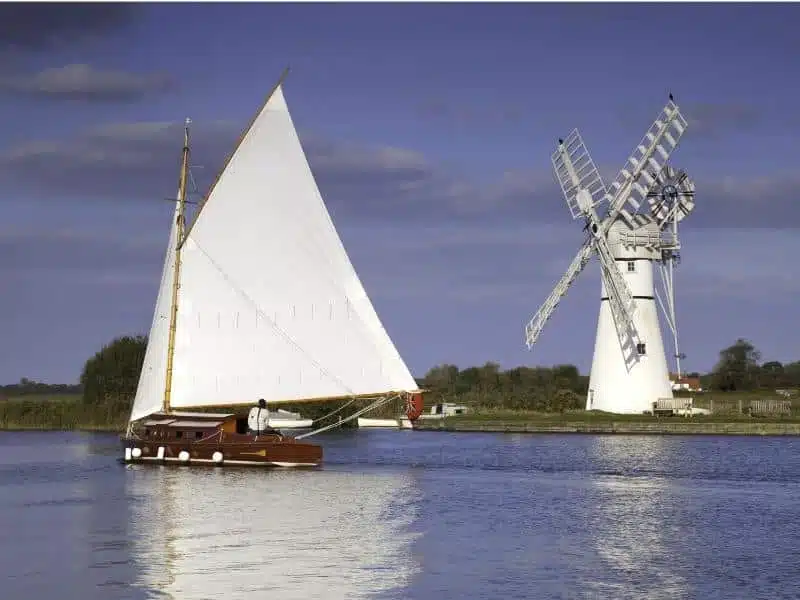 white sail on a wooden boat sailing past a white windmill