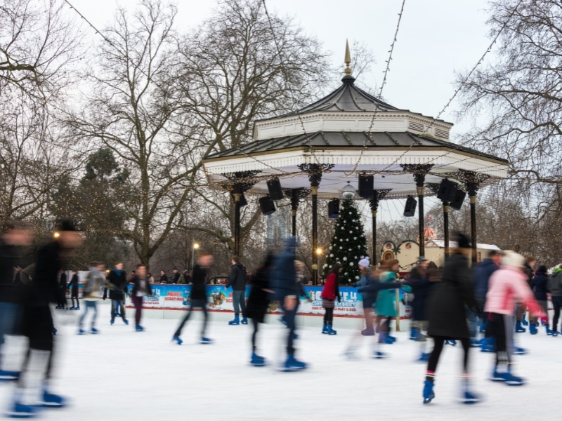 People ice skating around a bandstand with a Christmas tree in the background