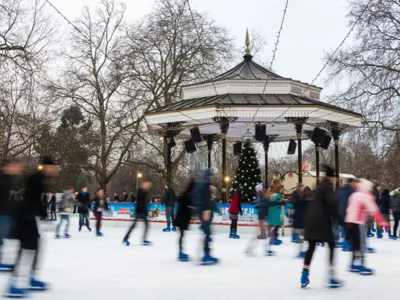 people ice skating around a bandstand with a christmas tree in the background