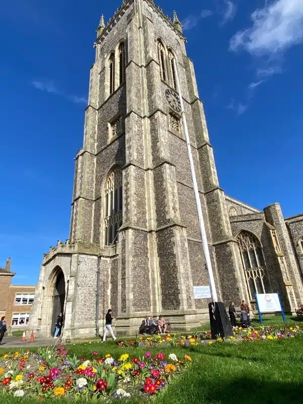 traditional stone church with a square tower surrouned by grass and spring flowers