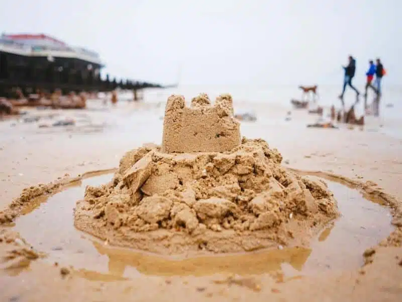 A seaside resort beach with sandcastle and dog walkers and pier in background 