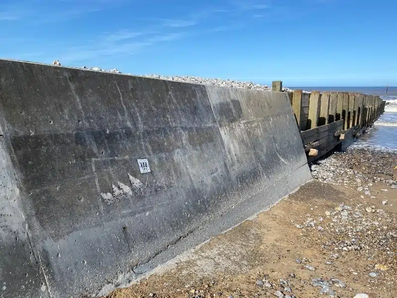 concrete and wooden groyne by a single beach with a small piece of art work painted on it depicting a row of crabs