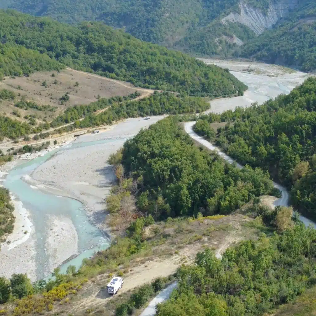 wide meandering turquoise rocky river surrounded by trees and a white camping car parked next to the river