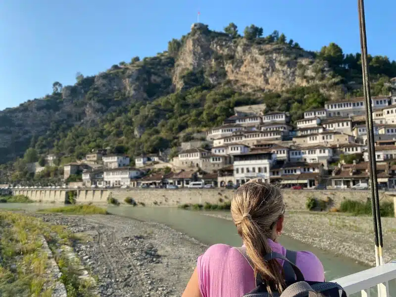 woman in a pink t-shirt looked across a river to white houses with many windows