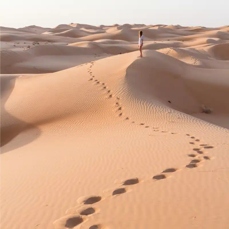 woman walking barefoot through sand dunes