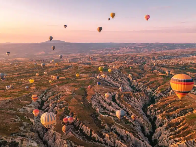 hot air balloons rising at dawn over a rocky landscape