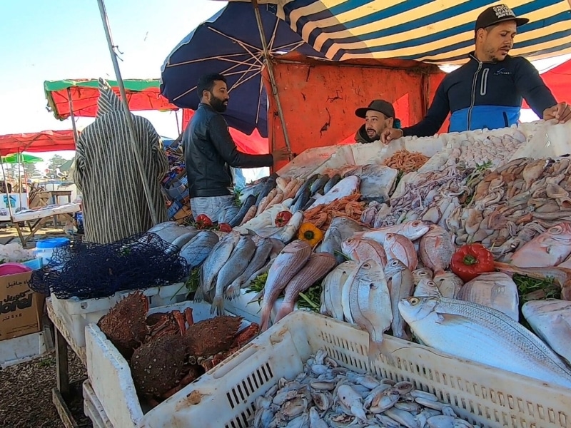 men selling fresh fish under a colorful canopy