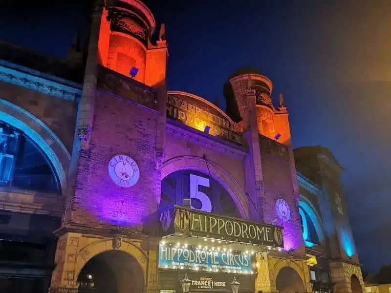 Front of large theatre building with turrets, lit with red and purple lights at night