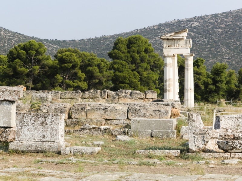 ancient columns and stone backed by green shrubby hillsides