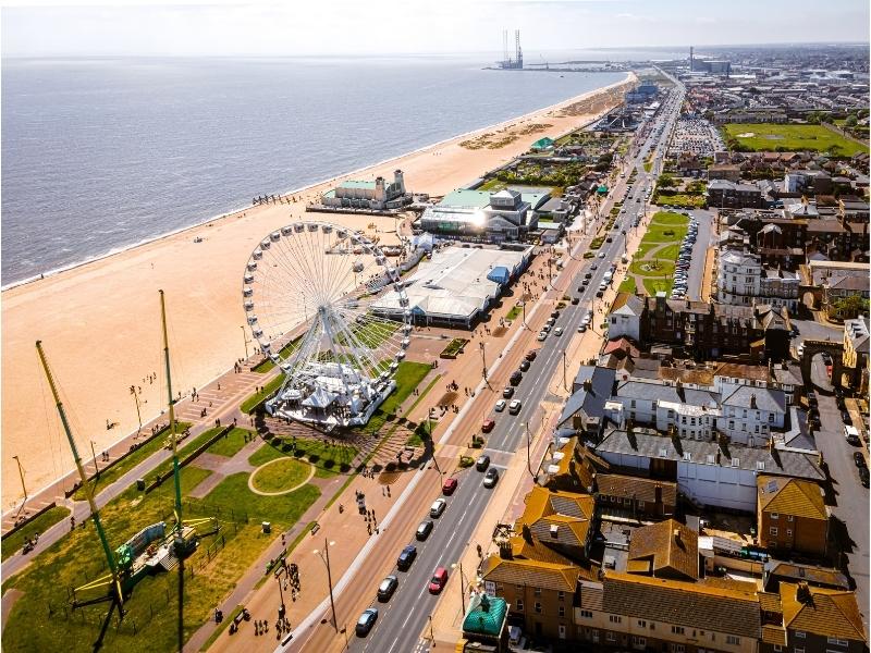 road running alongside a beach with fairground rides and buildings either side