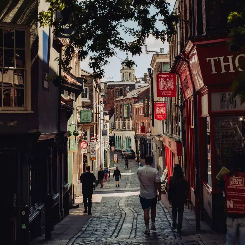 people walking down a cobbled street lined with shops