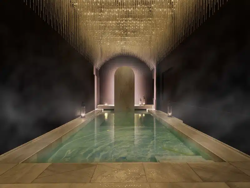 large stone bath of steaming water with an arch at one end of the room