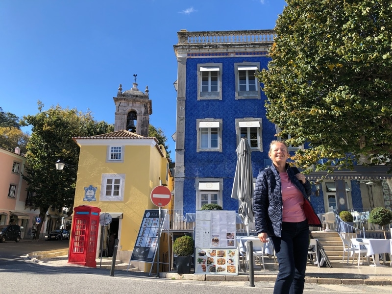 woman standing in front of yellow and blue houses with a red phone box in the front