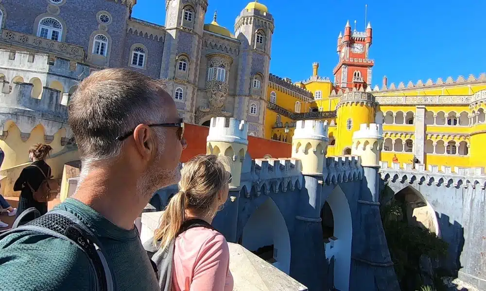 red and yellow turreted castle with people looking towards it over a crenellated wall
