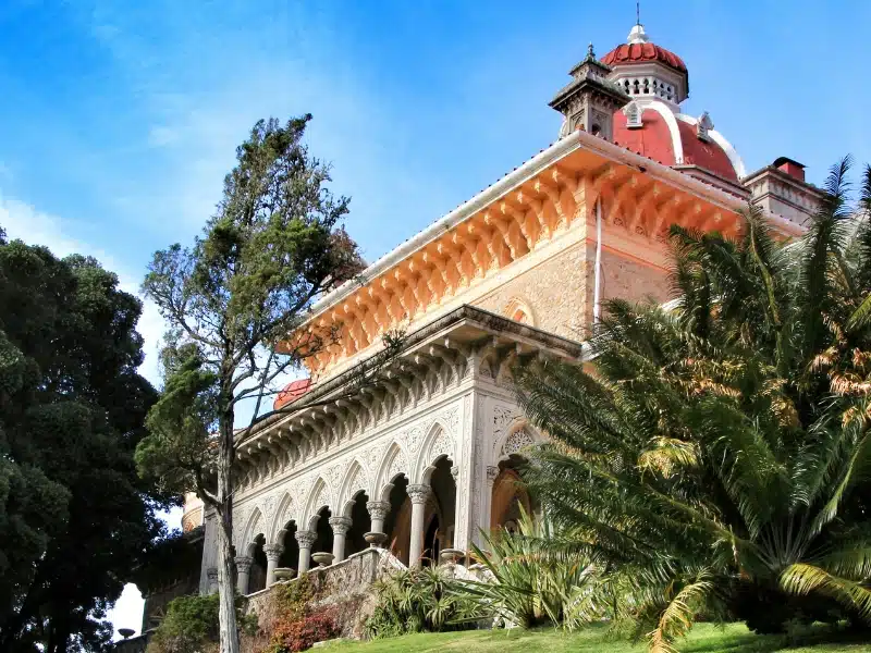 stony and peachy coloured building with ornate soffits and arces, surrounded by palms and trees