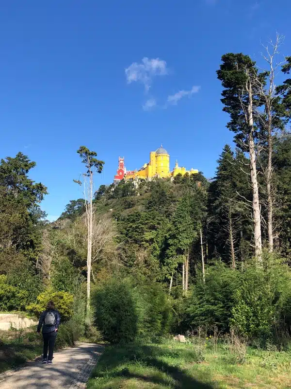 red and yellow palace high on a hill with a woman walking towards it on a lower path 