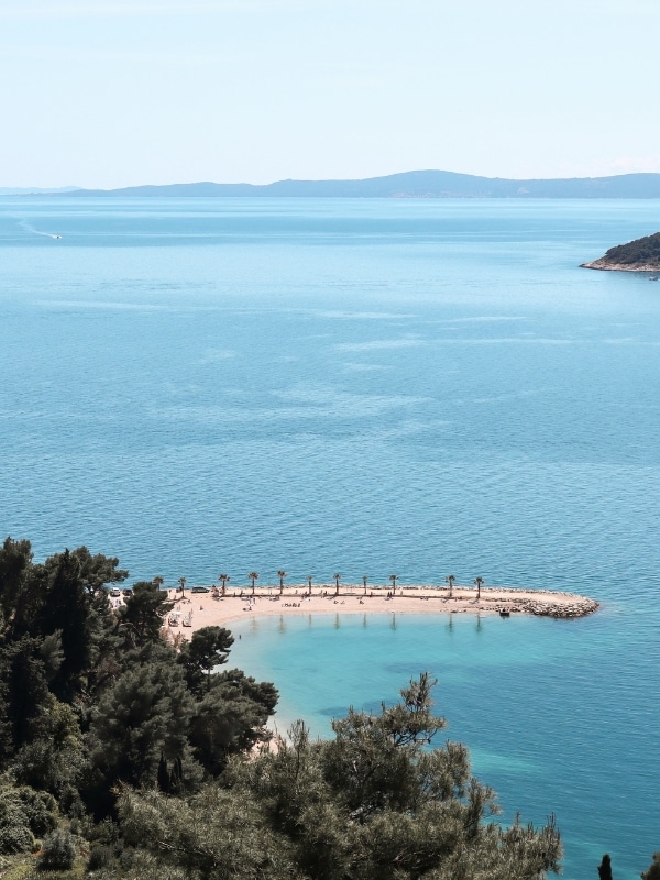 spit of land creating a small beach with path trees in a blue sea