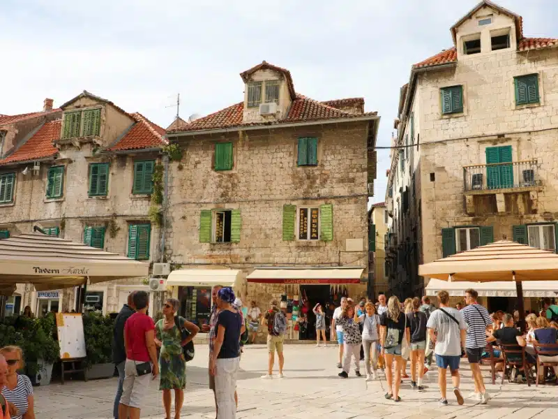 old stone buildings around a square with restaurants, shops and people